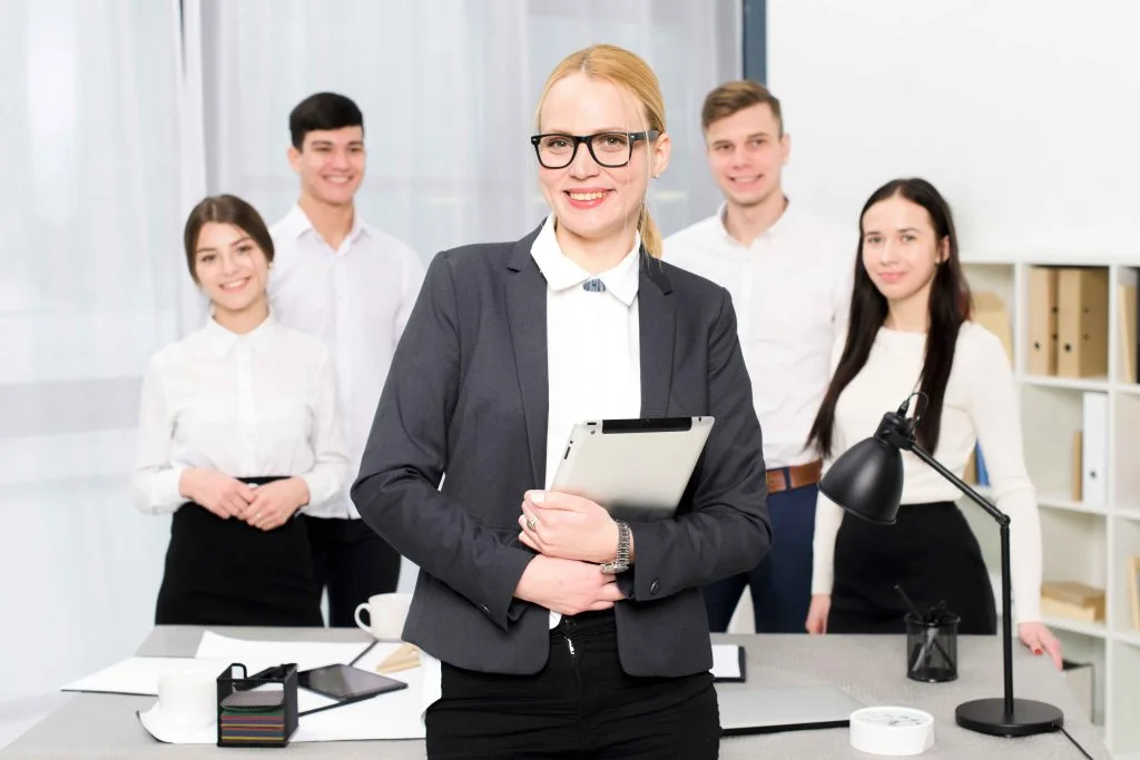 smiling-portrait-young-businesswoman-holding-digital-tablet-hand-standing-front-her-colleague